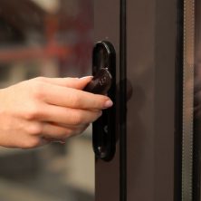 An image showing a hand turning a black handle on a bifolding door to open it.